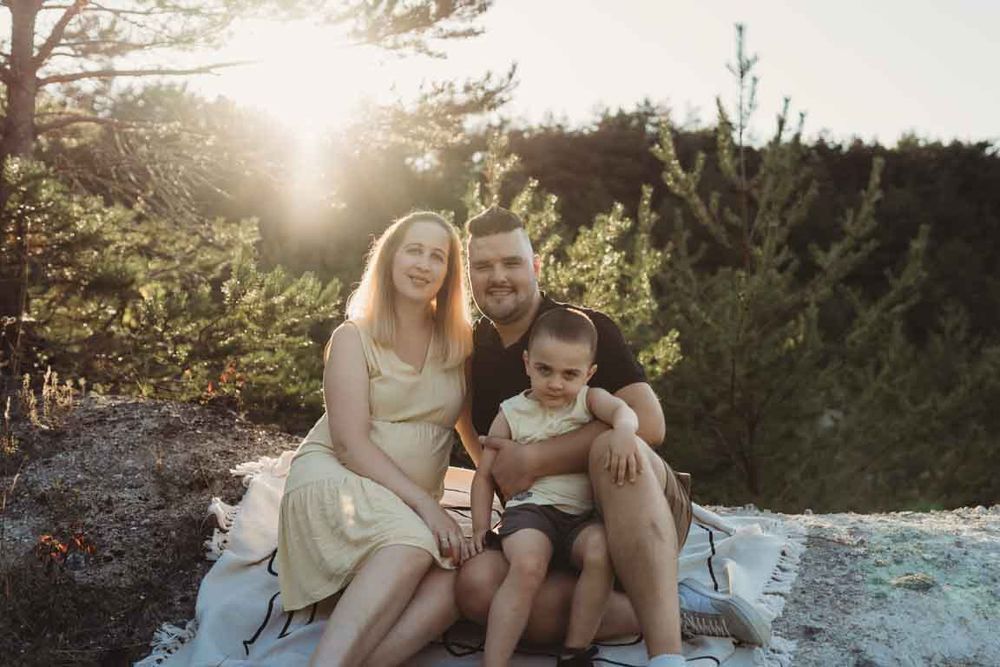 A cozy family enjoys a sunset moment together while sitting on a rocky outcrop surrounded by evergreen trees.