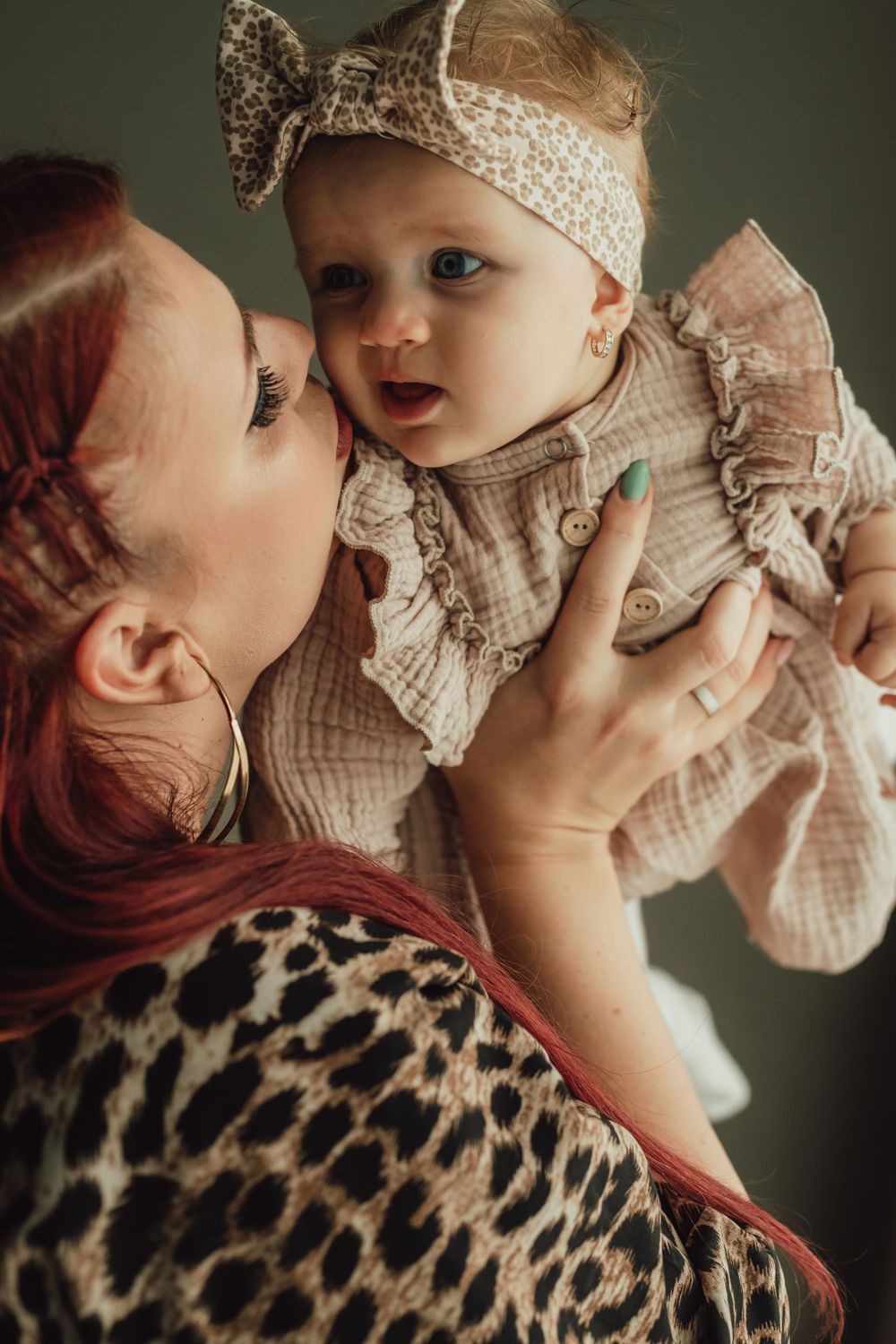 A tender moment between parent and baby wearing vintage-style clothing and a patterned headband.