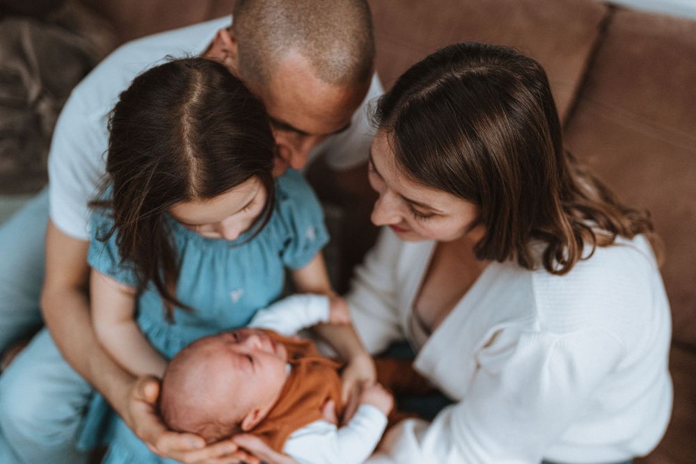 A tender family moment with a newborn baby being cradled and admired in soft natural lighting.