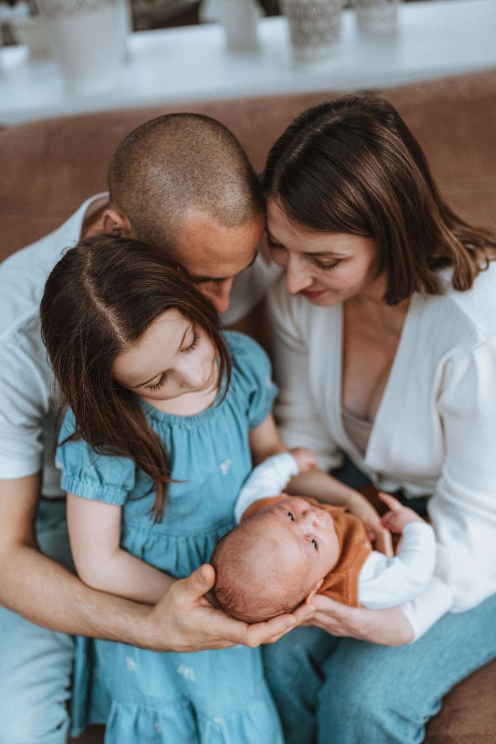 A family shares an intimate moment together while holding and admiring their newborn baby at home.