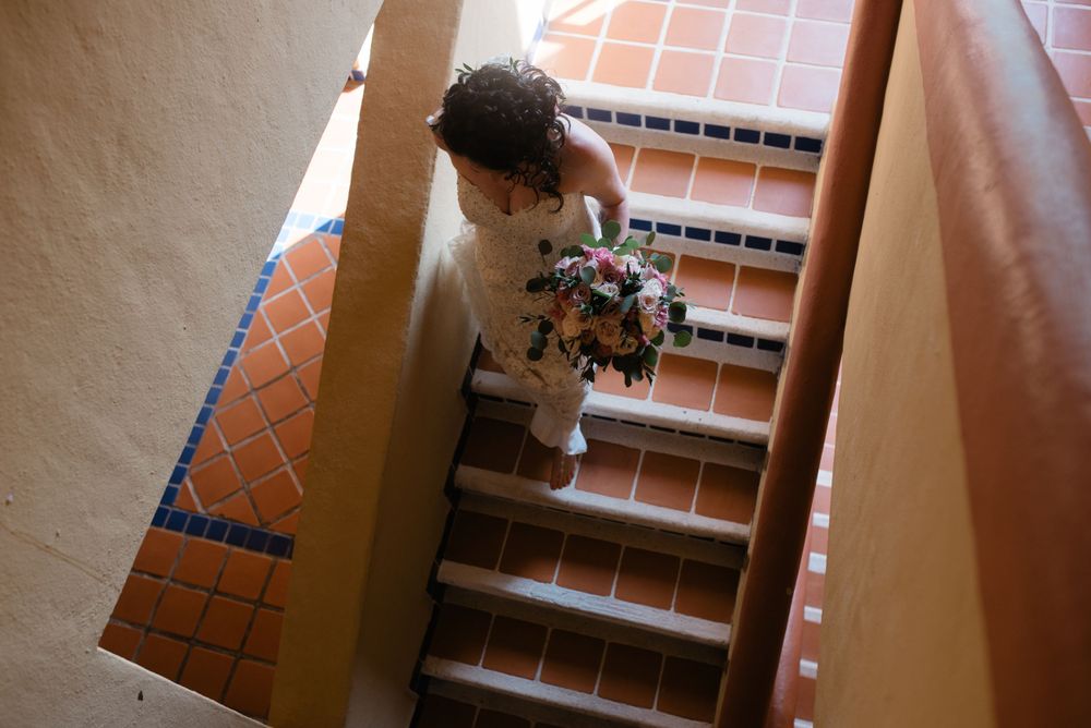Someone walks down terracotta tiled stairs in a stairwell while carrying flowers and looking down at their phone.