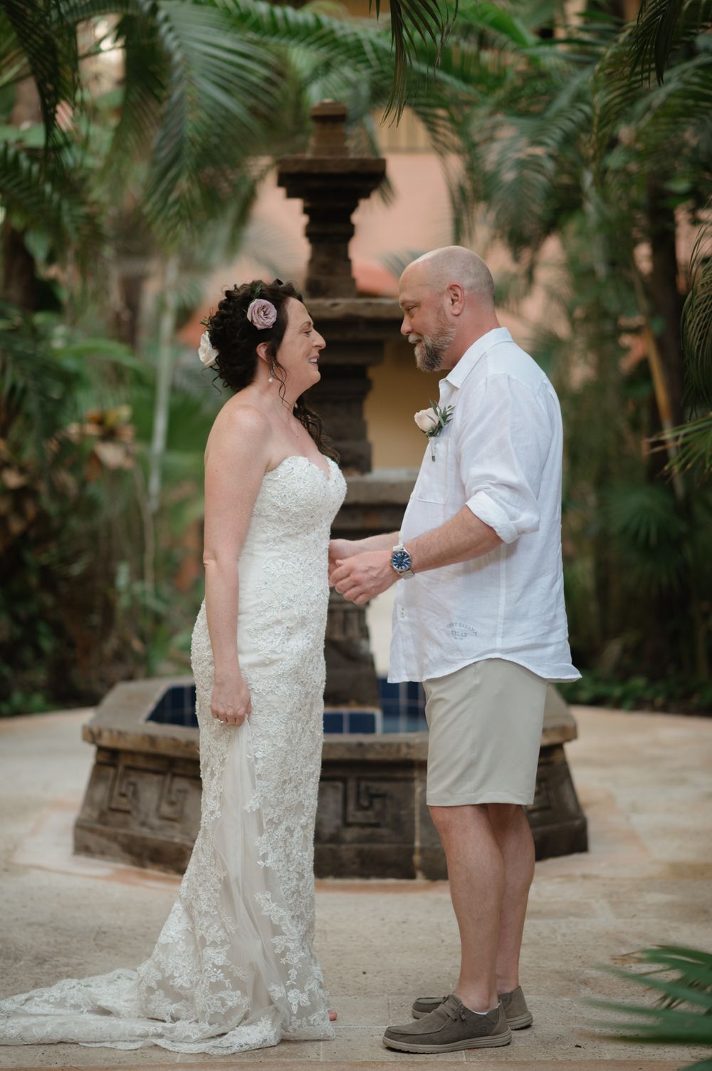 A couple shares a moment by a stone fountain surrounded by tropical palms at their wedding.