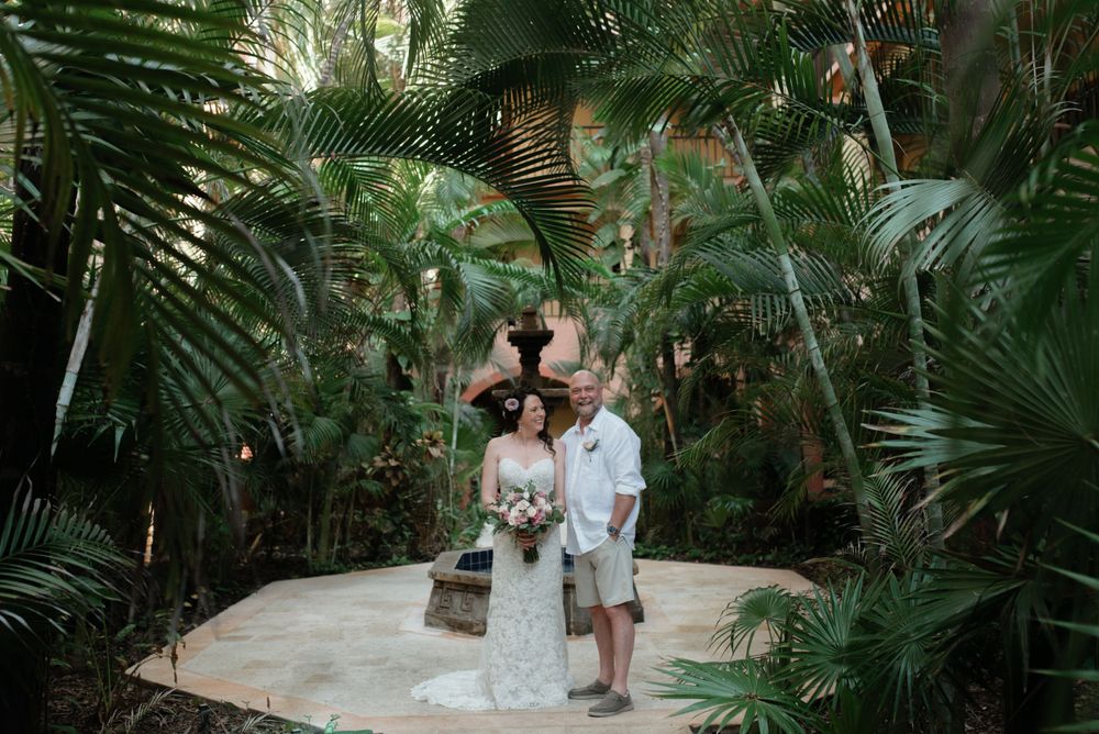 Two people stand on a stone pathway surrounded by lush tropical palm plants in an outdoor garden setting.