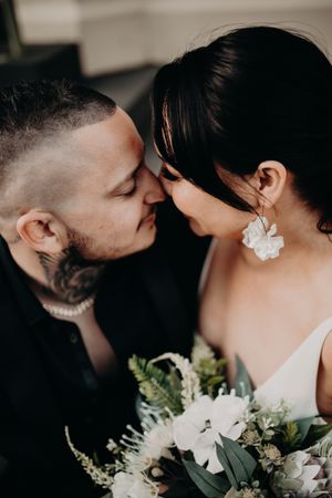 Intimate wedding moment with couple in close embrace while holding white and green floral bouquet.