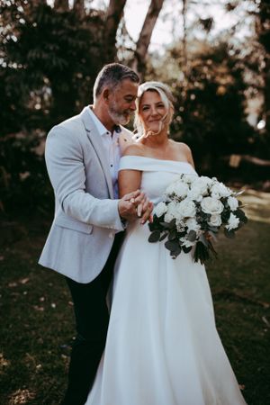 A loving couple shares an intimate moment at their outdoor wedding, with the bride holding a lush white bouquet.