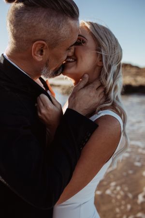 Intimate romantic moment captured between couple sharing a tender kiss on beach at sunset.