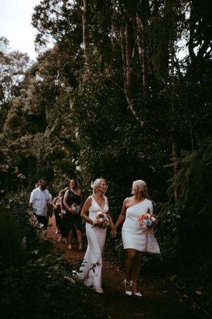 A wedding party walks through a scenic wooded path on a moody afternoon surrounded by tall trees.