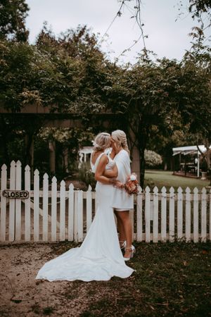 An intimate outdoor wedding moment by a white picket fence surrounded by lush greenery and trees.