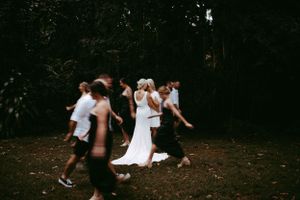 Wedding party dances together in a playful moment on a dark wooded path during outdoor celebration.