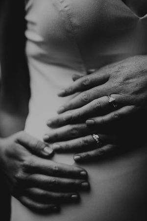 A black and white close-up photograph of hands adorned with rings gently resting against a torso.