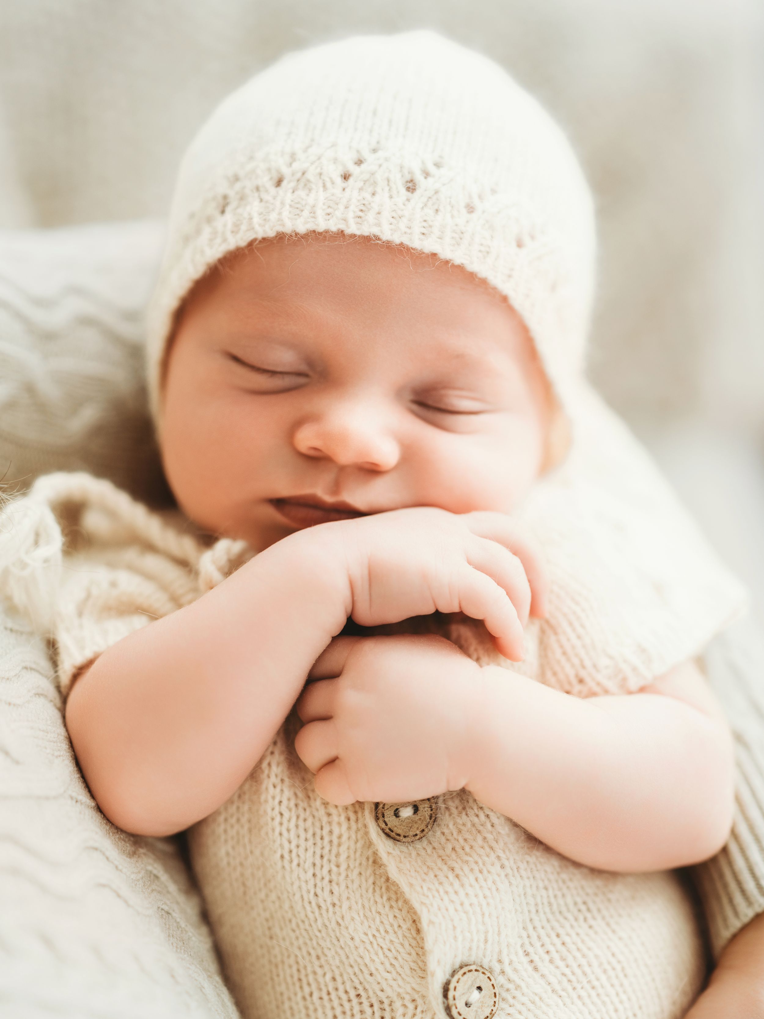 Peaceful sleeping newborn wearing cream knitted bonnet and cardigan - Bellevue baby photography session.