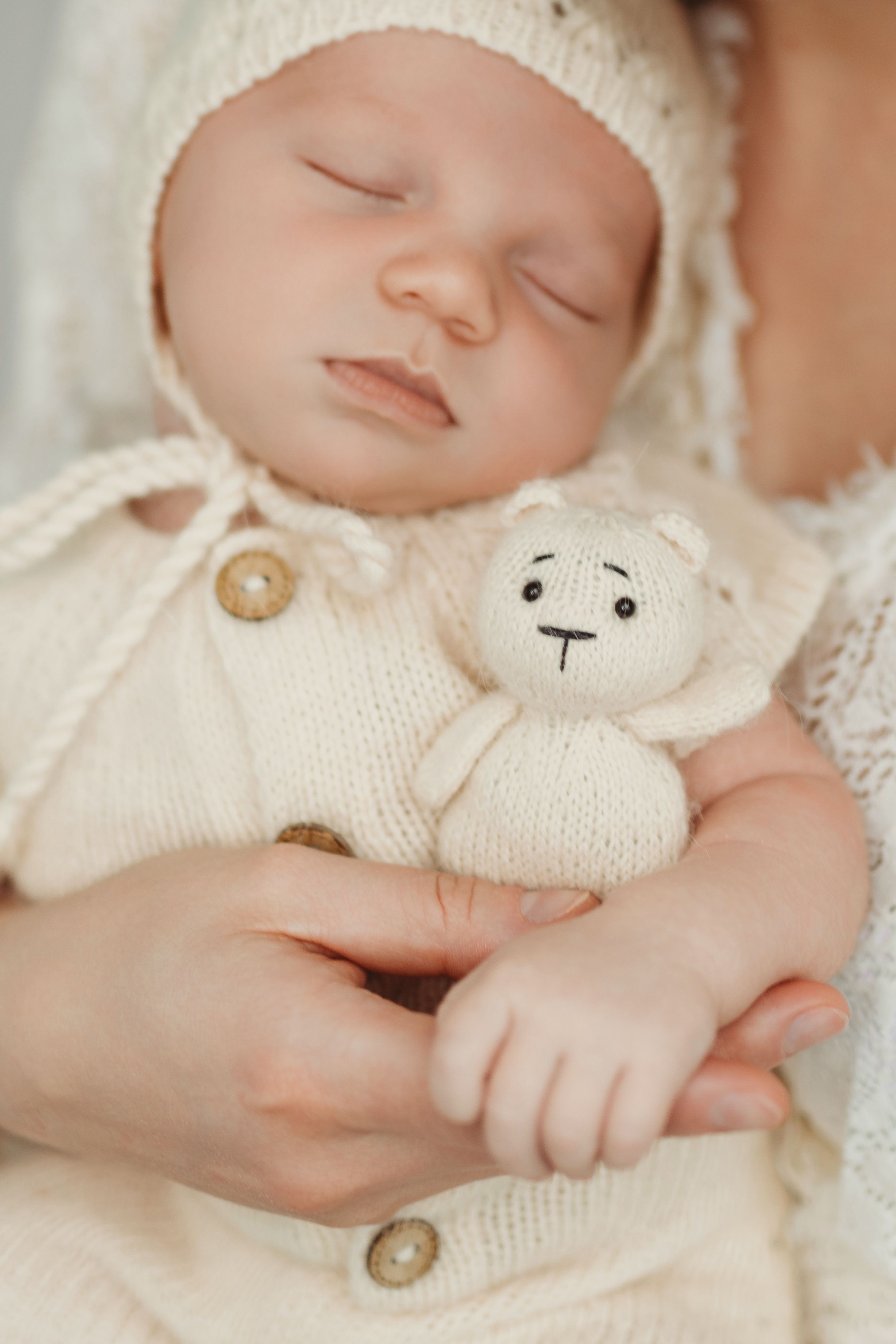 Peaceful sleeping newborn in white knit outfit holding small white teddy bear - Bellevue newborn photographer.