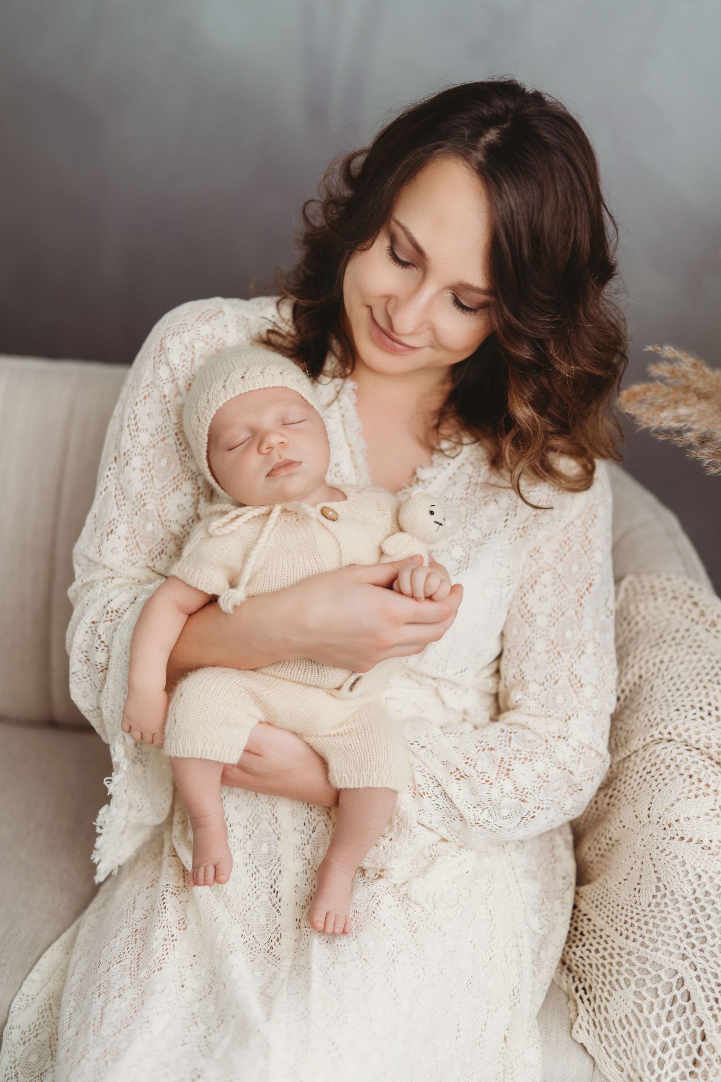A tender moment shows a woman in white lace dress holding a sleeping newborn baby dressed in cream-colored clothing. | Bellevue, WA