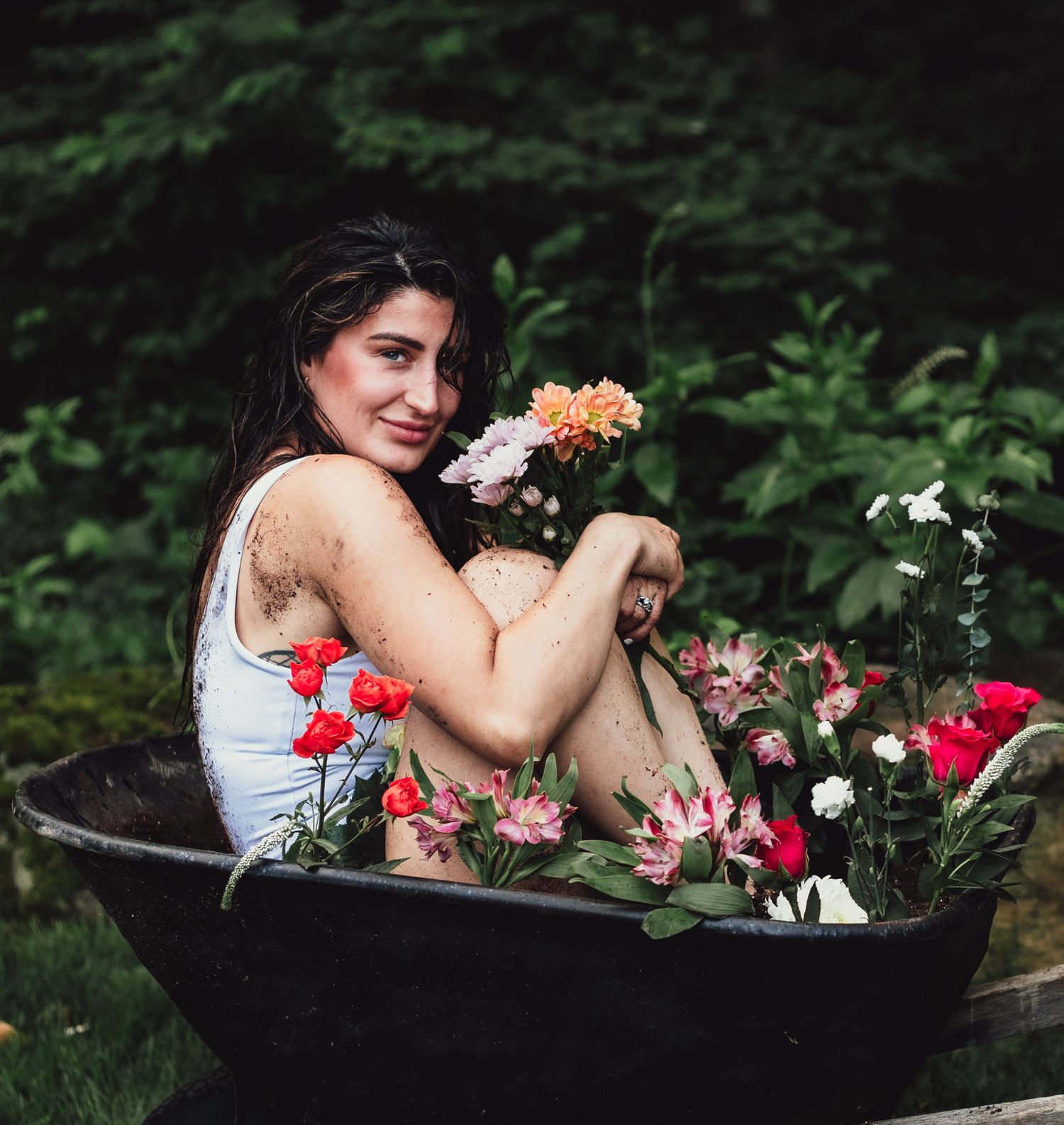 woman in wheelbarrow holding flowers, emotional, raining, garden, dramatic, lifestyle, creative photoshoot, themed