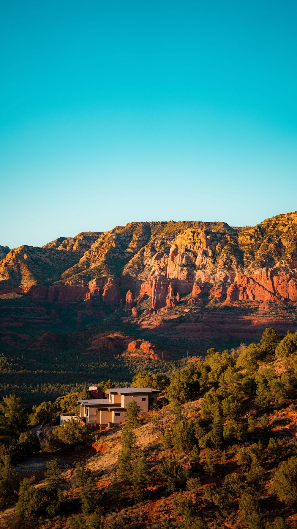 Red rock formations and desert landscape with modern house perched on hillside in Sedona.
