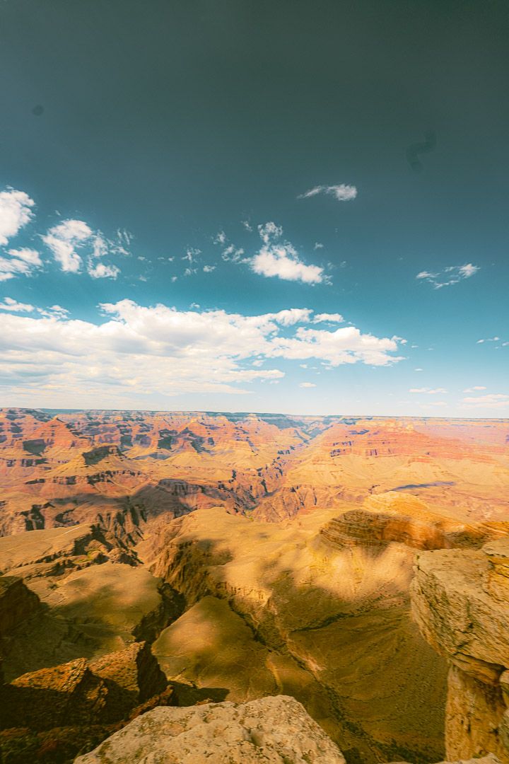 Stunning aerial view of the Grand Canyon's orange rock formations under bright blue skies with scattered white clouds.