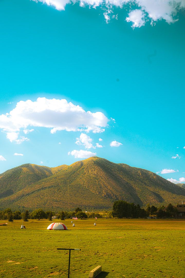 Two camping tents set up in a vast meadow with golden mountains rising against a bright turquoise sky.