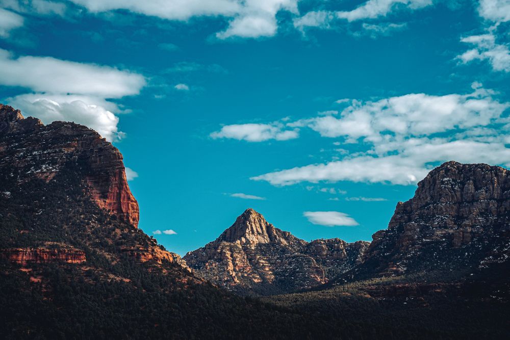 Majestic mountain peaks with dramatic cloud formations against bright blue sky.