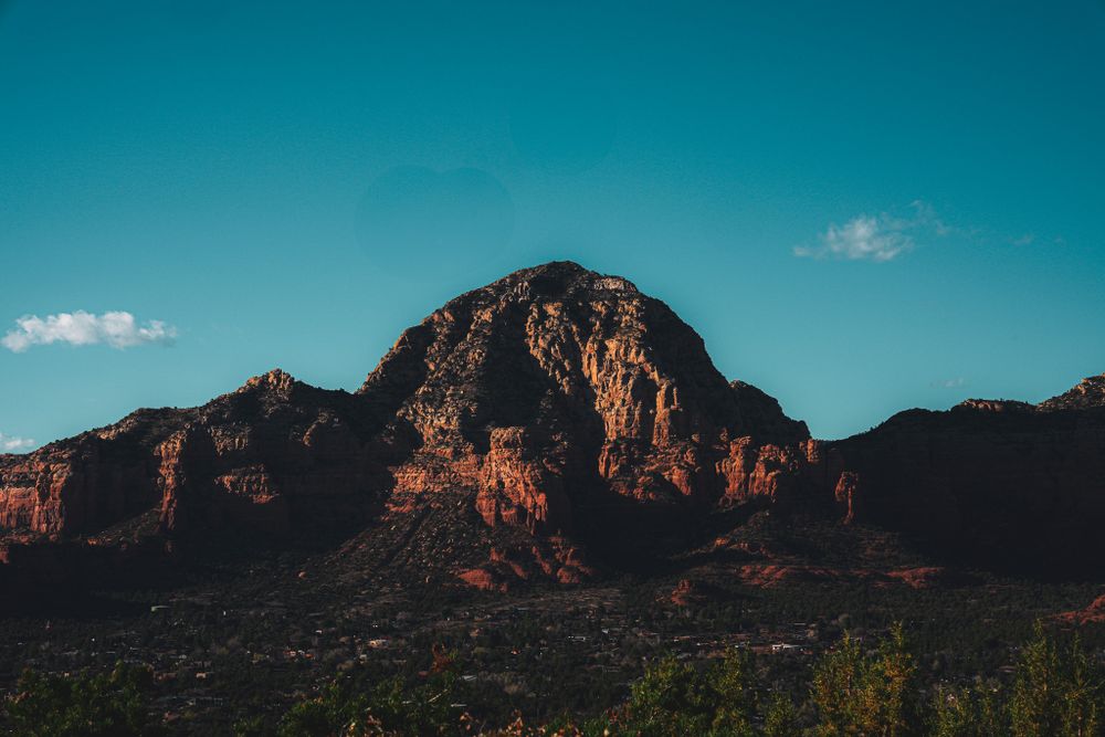 Rugged red rock mountain formation towers over Sedona's desert landscape under clear blue skies.