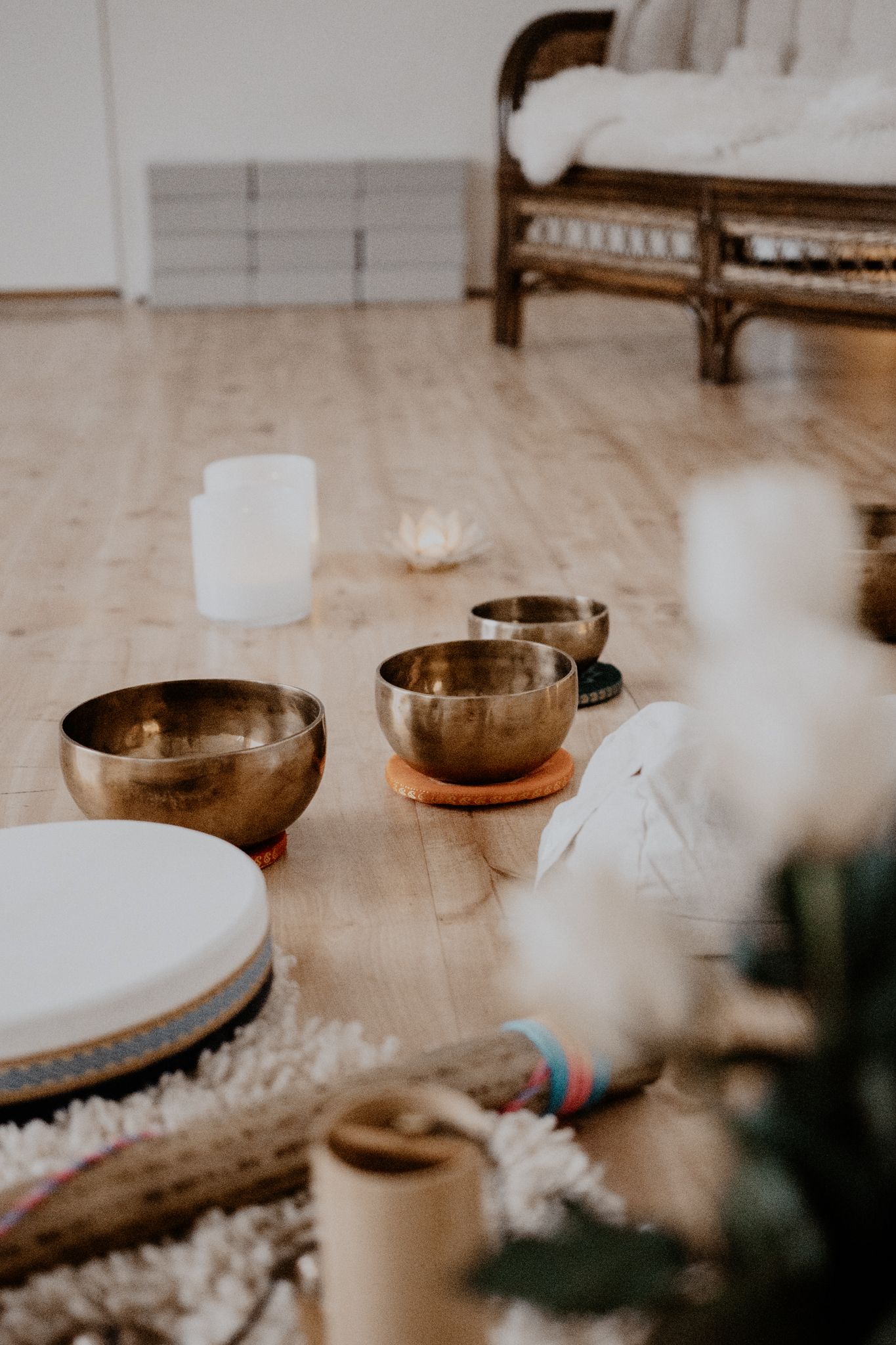 Peaceful meditation setup with singing bowls, candles and textured pillows on wooden floor in neutral tones.