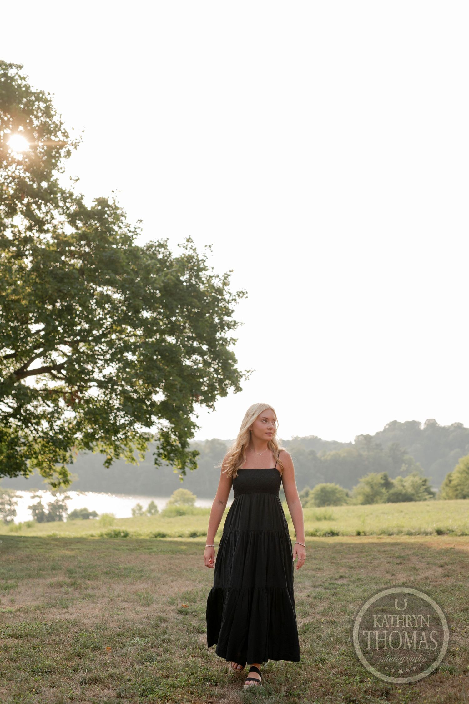 Long black dress photographed in evening light with tree silhouette against bright sky.