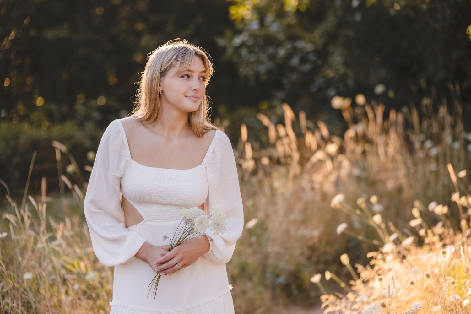 Woman in white dress with puffy sleeves poses in golden field at sunset.