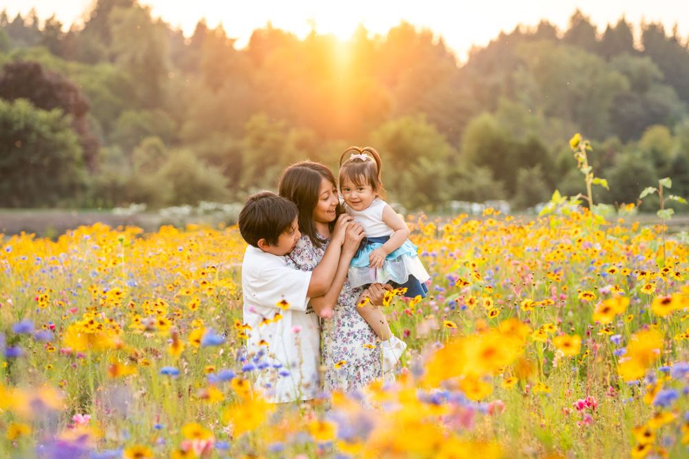 Siblings holding baby sister in a field of wildflowers at sunset in JB Family Growers.