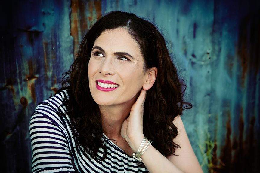Lifestyle close-up portrait taken on Myer St. in Tucson, AZ . Woman wears a black and white striped shirt against a teal textured backdrop.