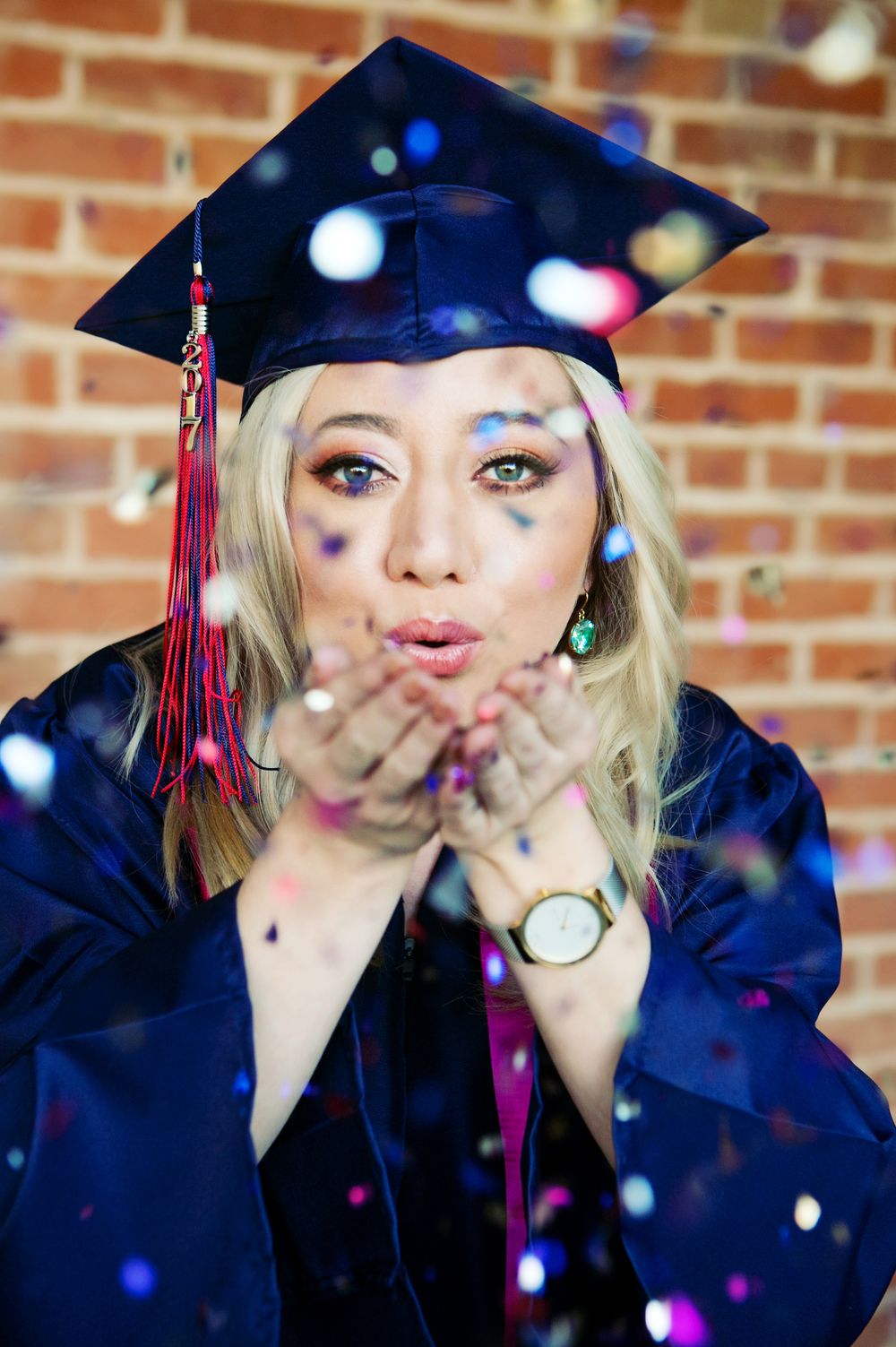 University of Arizona senior picture.  A girl wearing navy blue graduation cap and gown, blowing confetti at the camera.