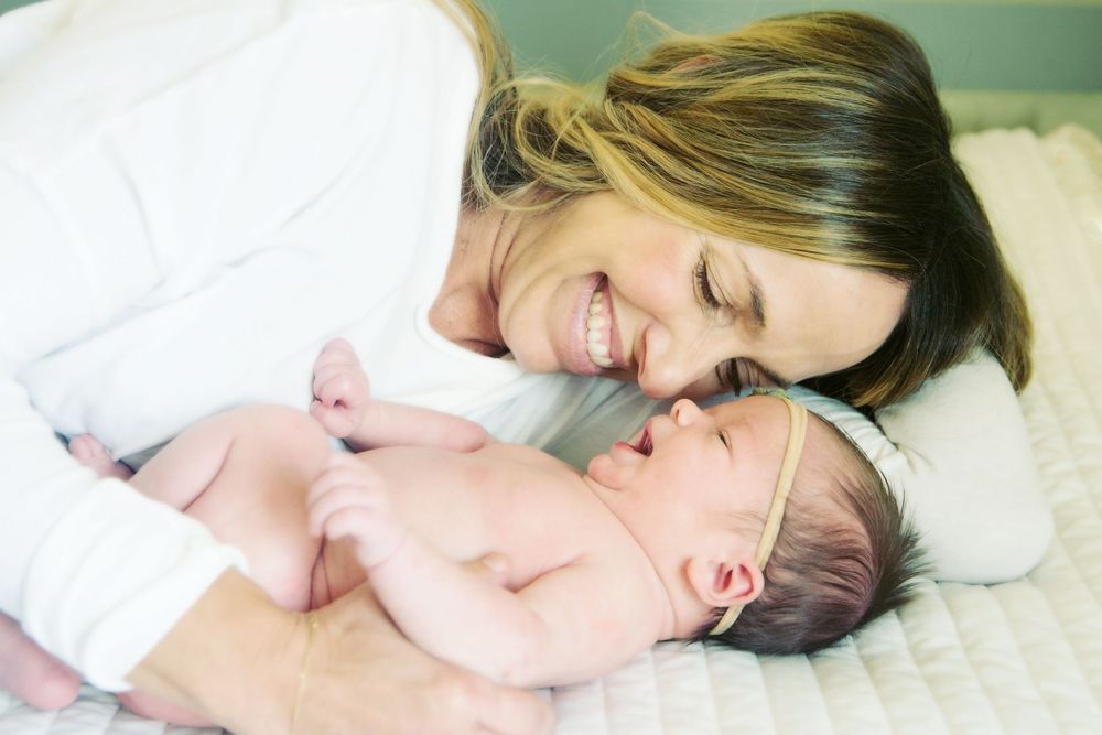 A close up portrait of a beautiful mother laying down with her two week old newborn baby.  Newborn photograph taken on white blanket.