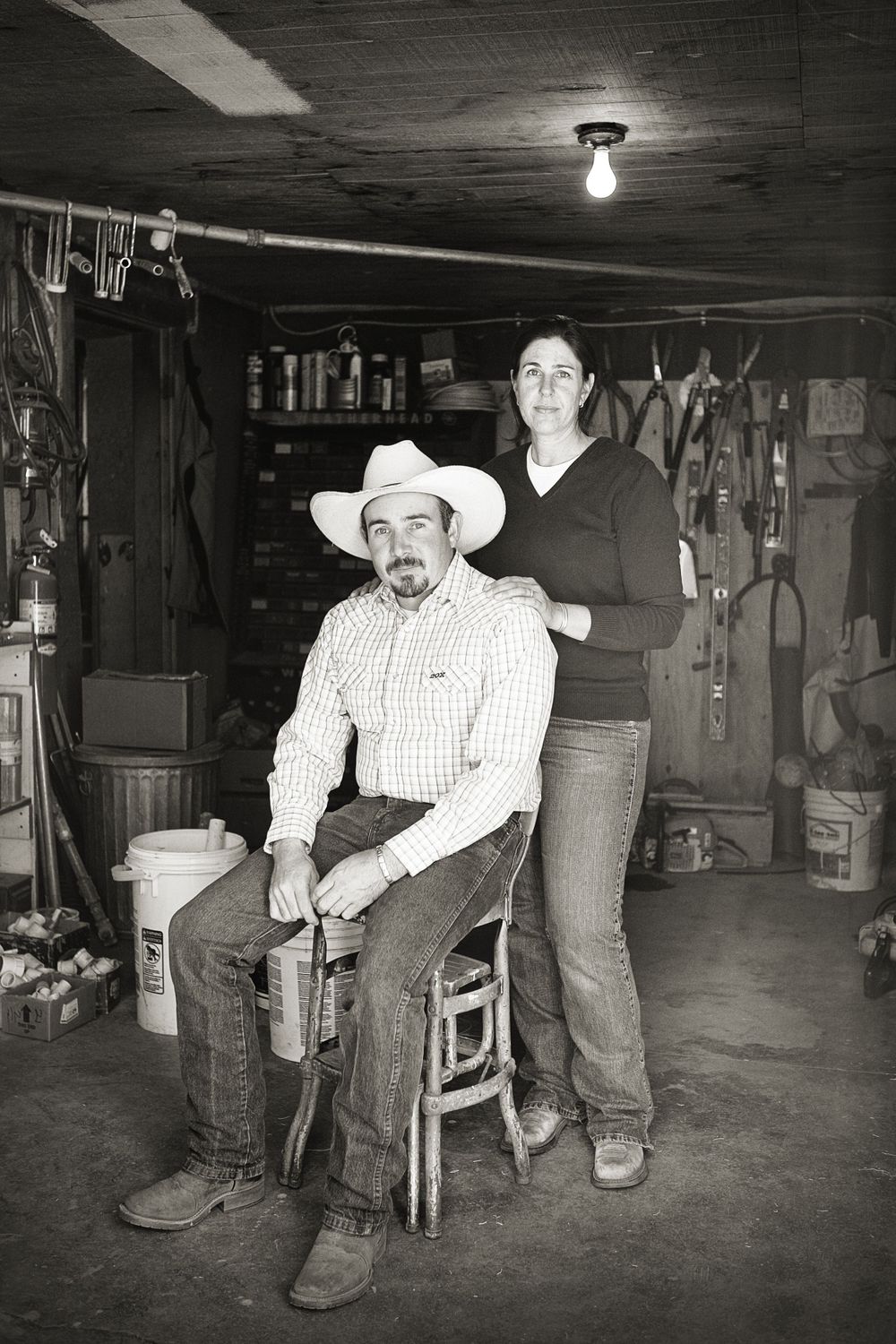Black and white engagement photo inside a barn or storage room showing a cowboy and cowgirl with rustic decor in Sonoita, AZ.