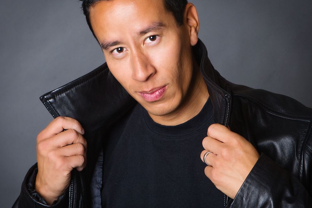 Portrait in Tucson, AZ against gray studio background with dramatic lighting.  Male subject is wearing black leather jacket and dark shirt.