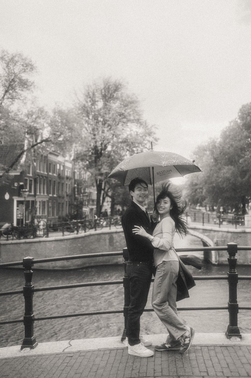 Two people share an umbrella on a rainy day by Amsterdam's canal.