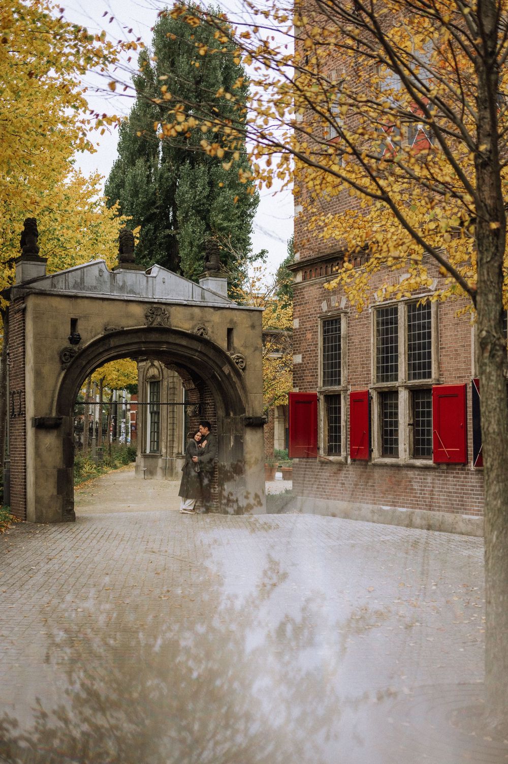 Historic brick building with red shutters and autumn trees in Amsterdam.