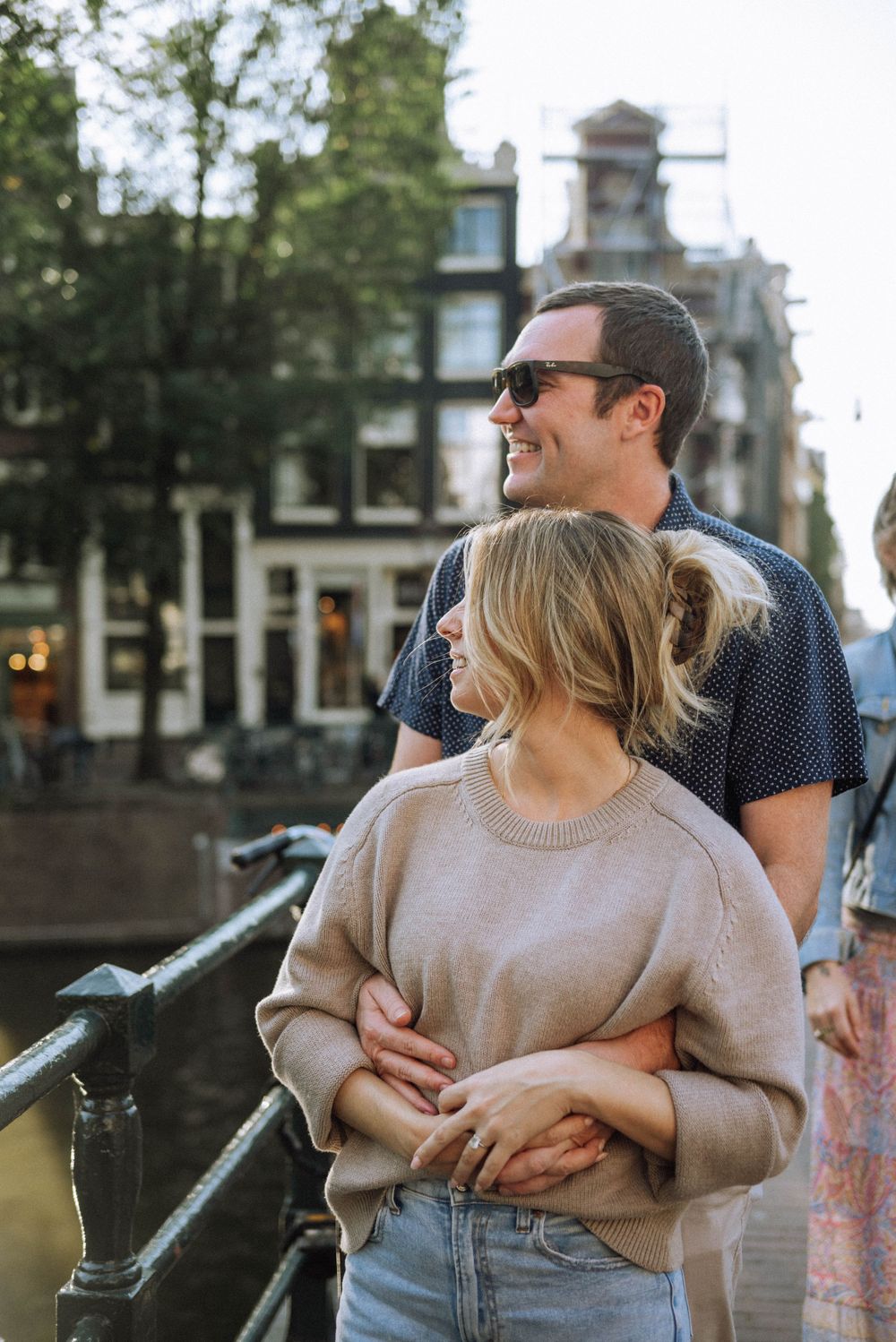 Happy couple laughing together by a canal with historic buildings in the background.