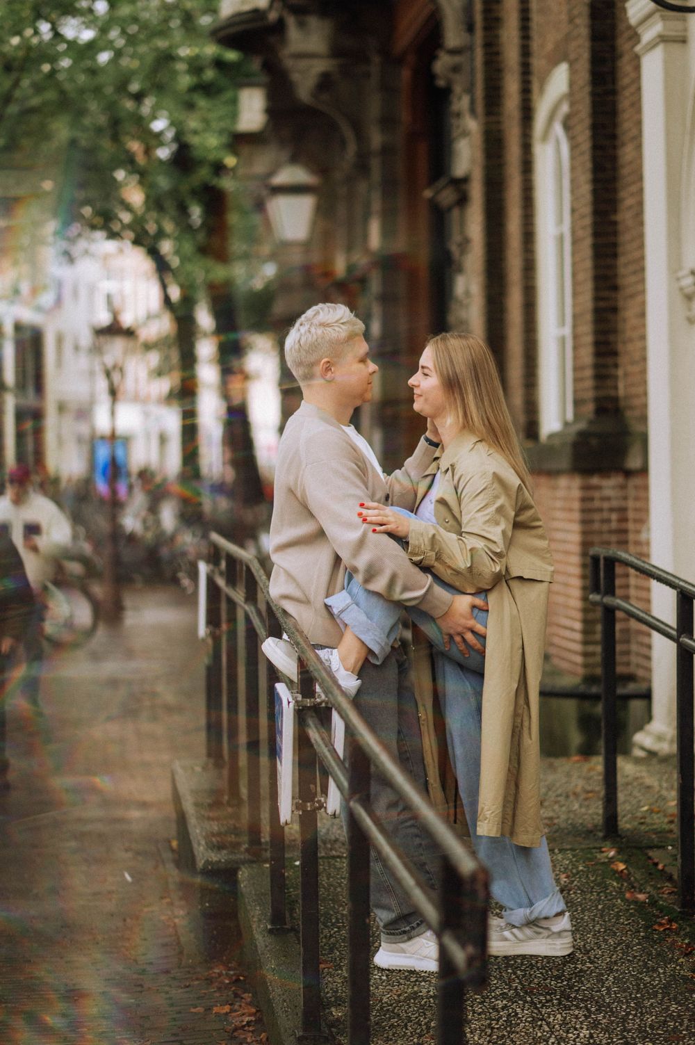 Couple shares playful moment along tree-lined brick pathway.