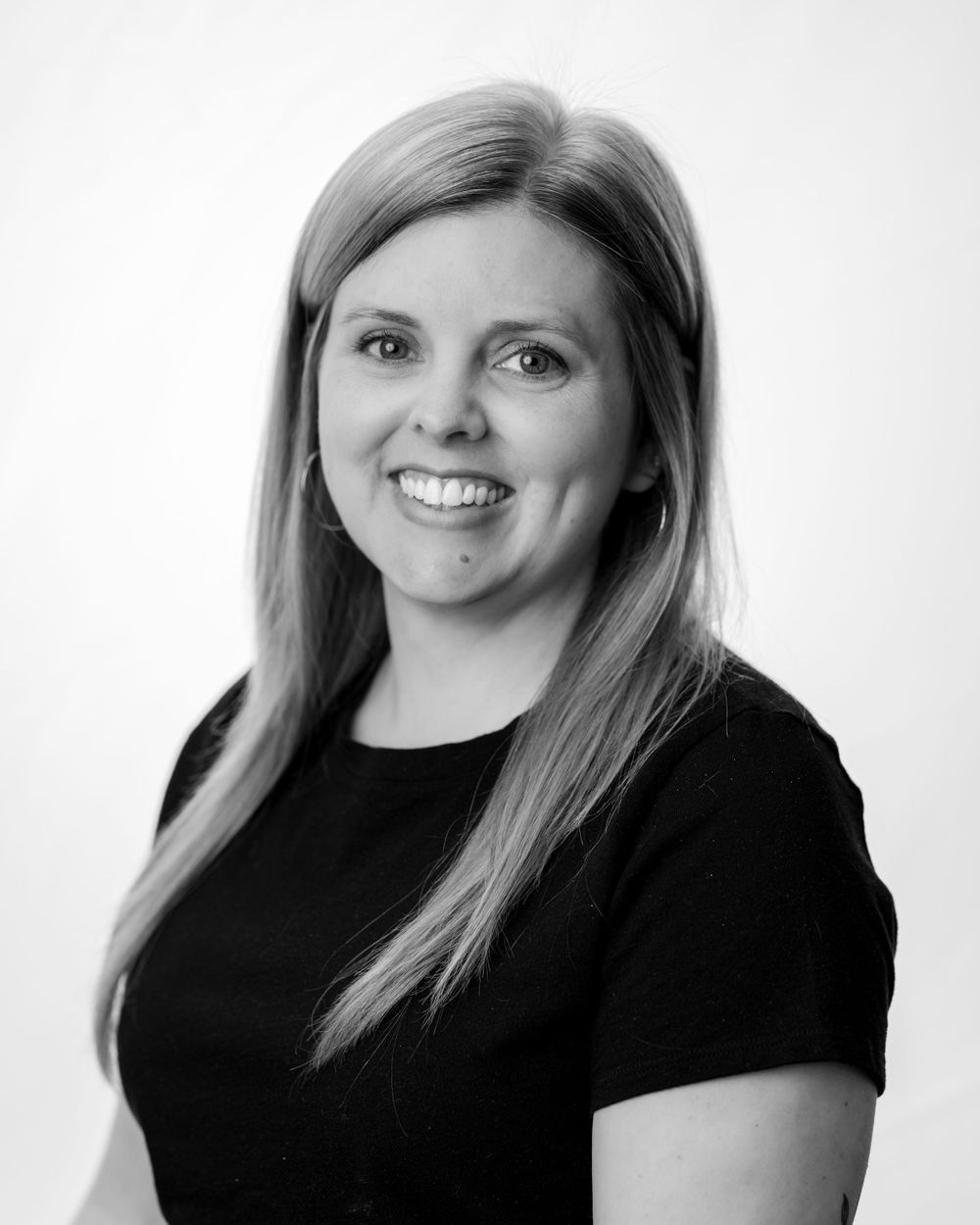 Professional black and white headshot portrait of a smiling person with long blonde hair wearing a black top.