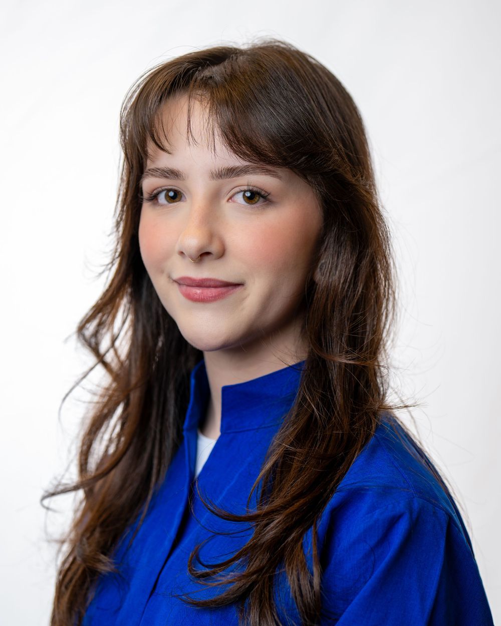 Professional portrait of a young person with long brown hair wearing a bright blue blazer against a white background for a clean headshot.