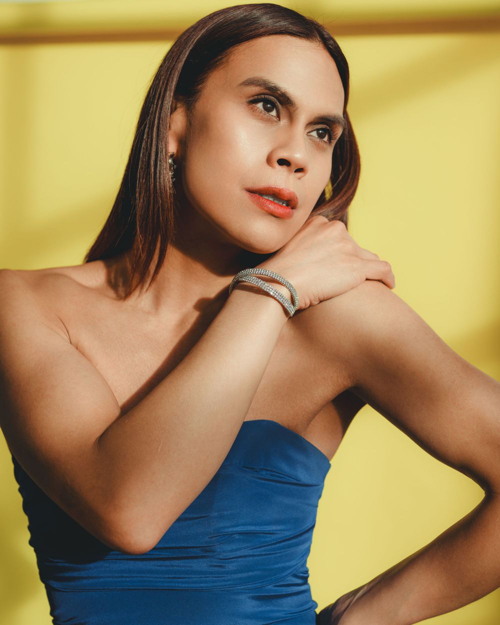 Fashion photo featuring a person with long dark hair in a strapless blue dress against a yellow background creating a cinematic photograph.