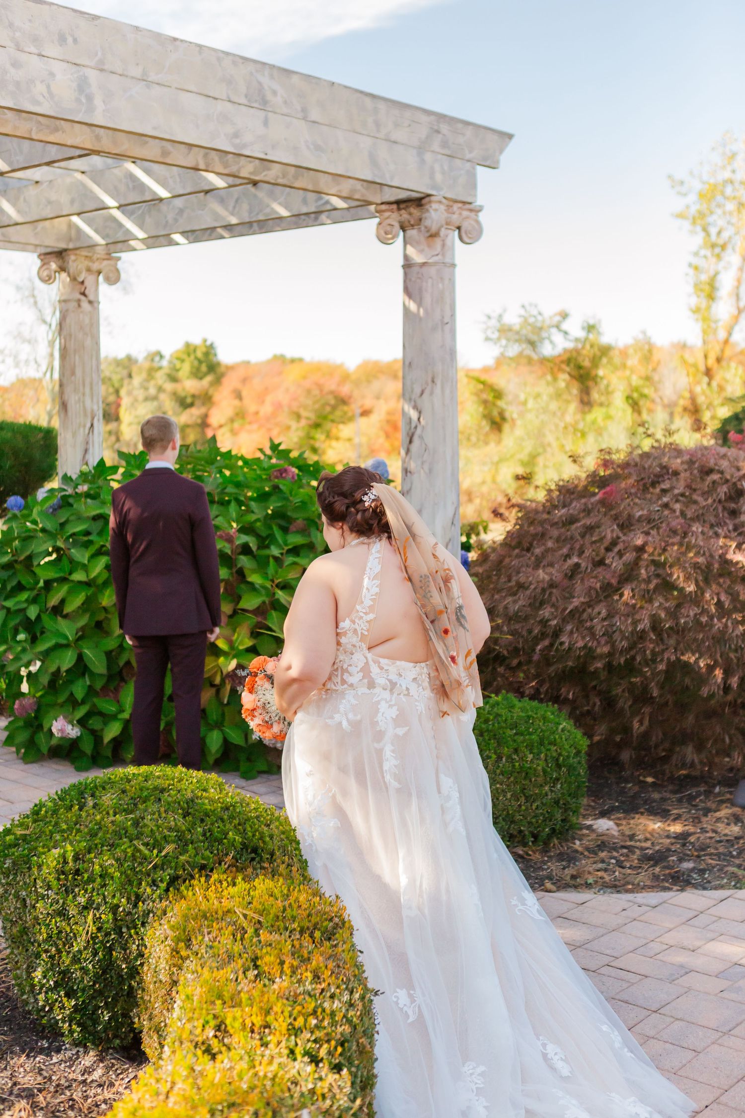 Couple standing under white pergola during first look moment at garden wedding.
