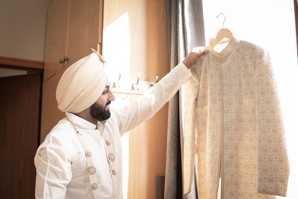 A person in white traditional attire adjusts clothing near a window.