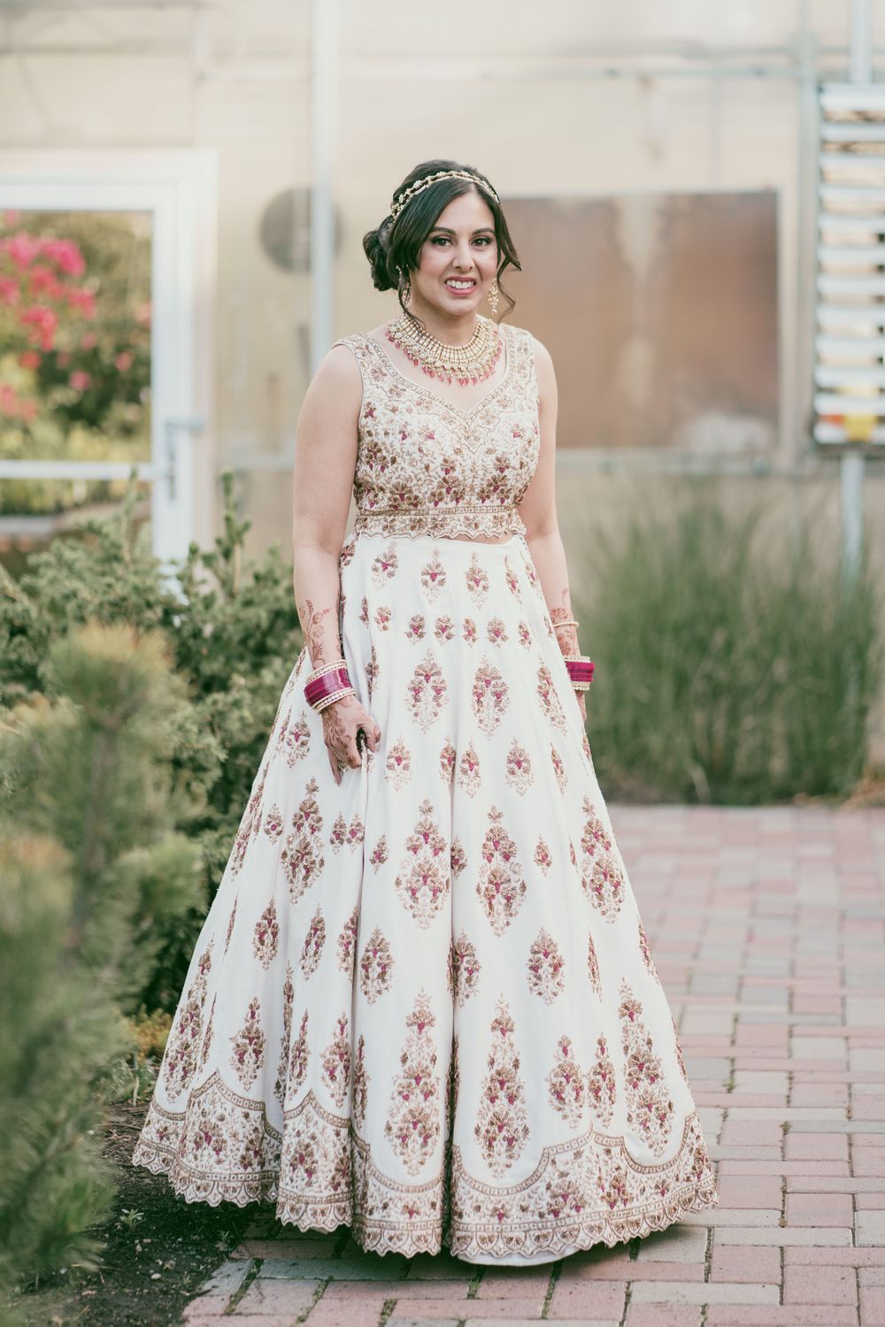 A stunning full-length portrait of a bride in an embroidered white and gold lehenga with matching accessories.