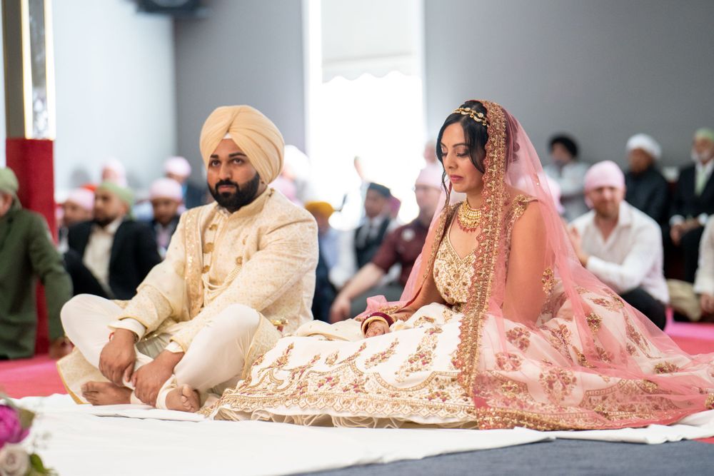 A traditional Sikh wedding ceremony with couple seated on floor in matching cream outfits.