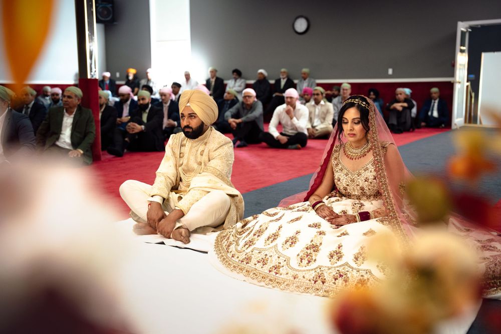 A traditional Sikh wedding ceremony takes place on a red carpeted floor with attendees seated in traditional attire.