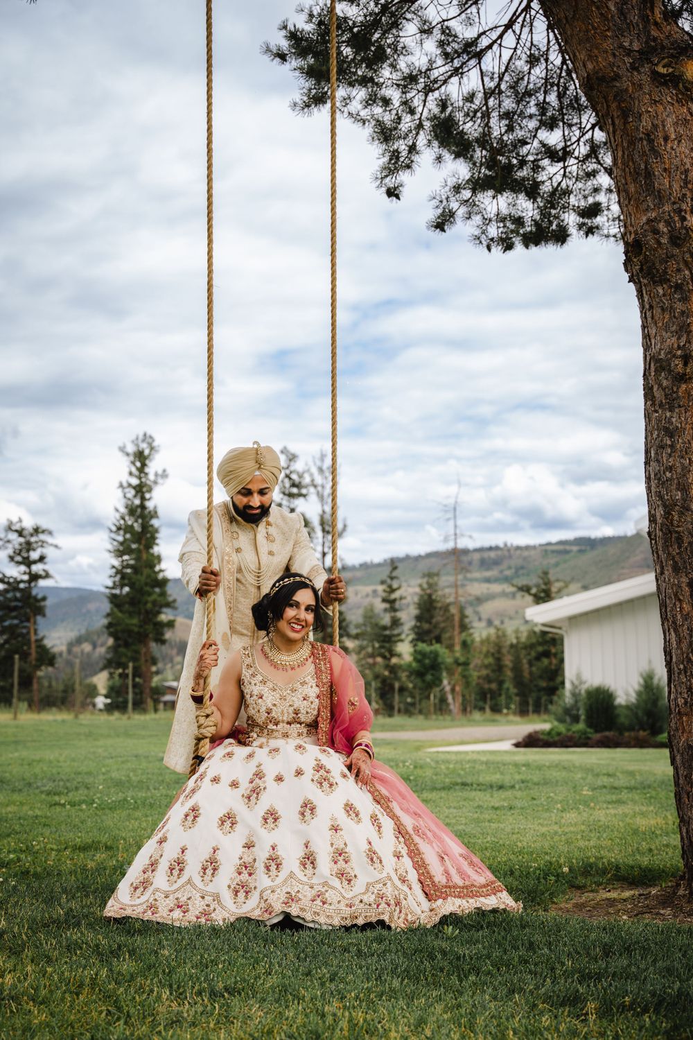 A romantic couples photo on a tree swing with mountain landscape backdrop.
