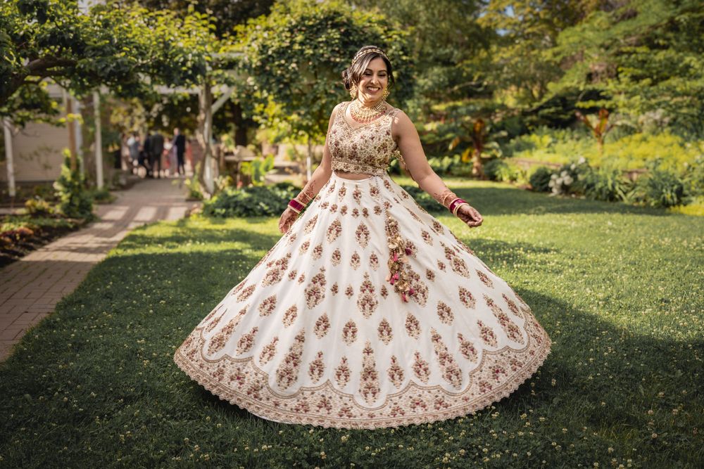 A beautiful white and gold lehenga dress twirls in a lush garden setting.