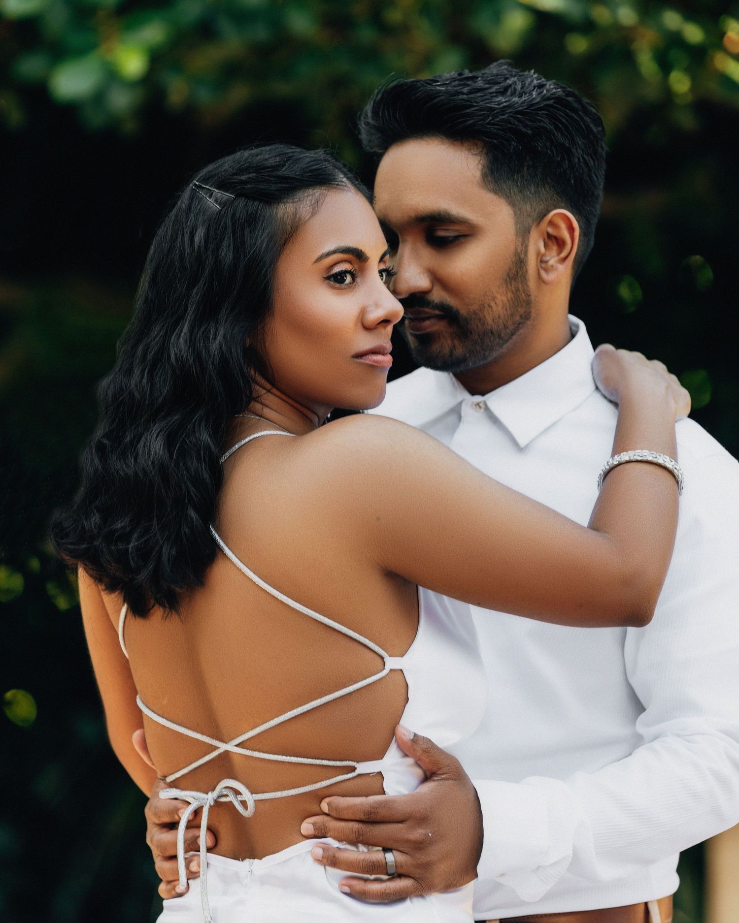 A couple embraces in a romantic outdoor portrait with lush greenery.