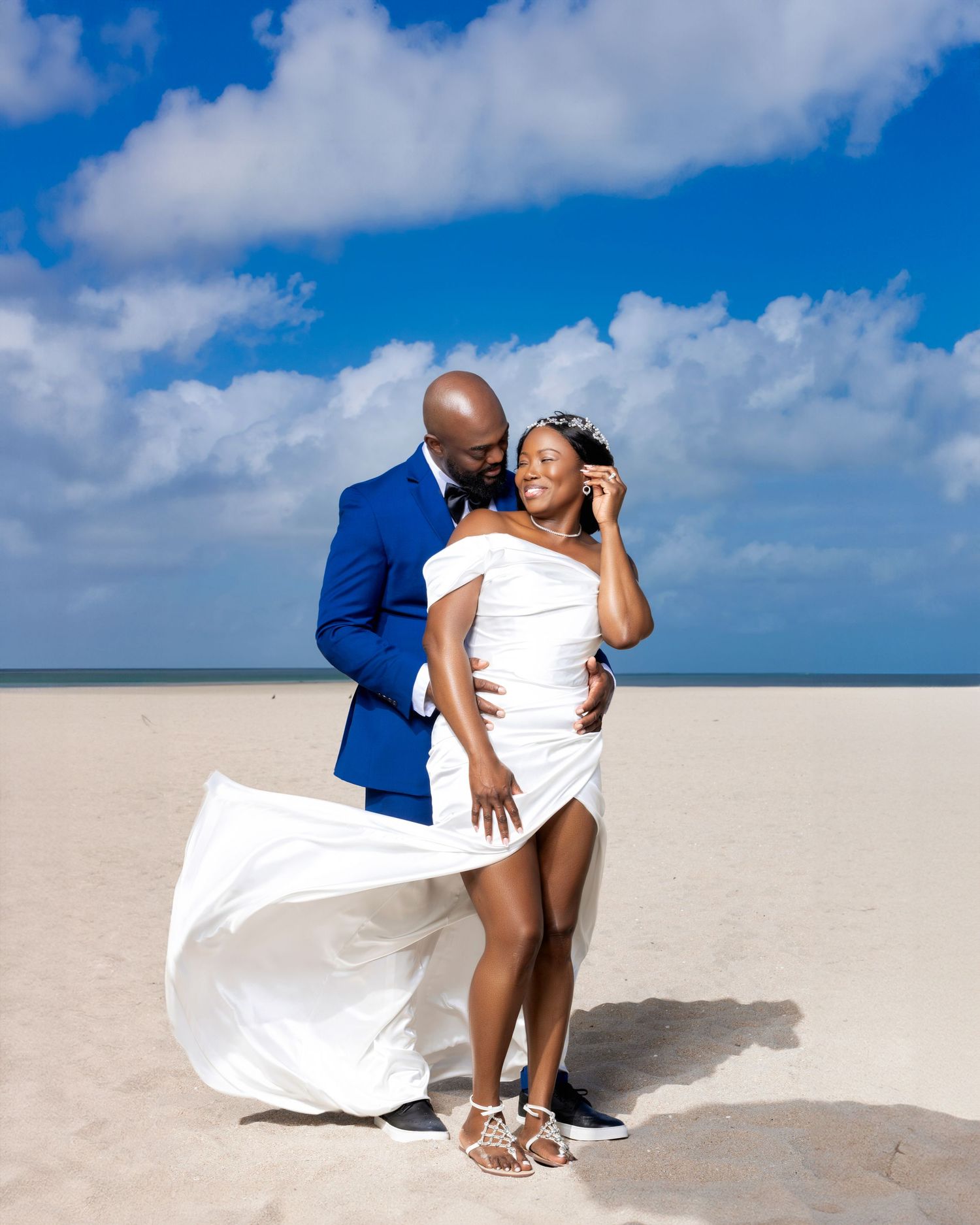 Romantic beachside portrait with flowing white dress against blue sky.