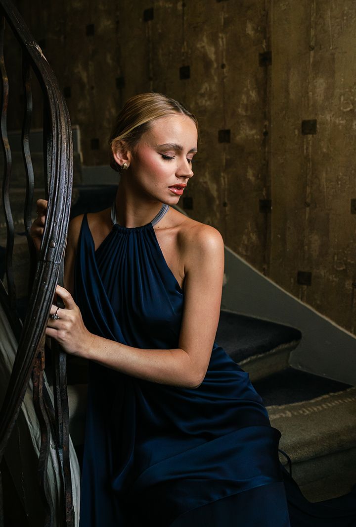 Elegant navy blue evening gown photographed on vintage staircase with moody lighting.
