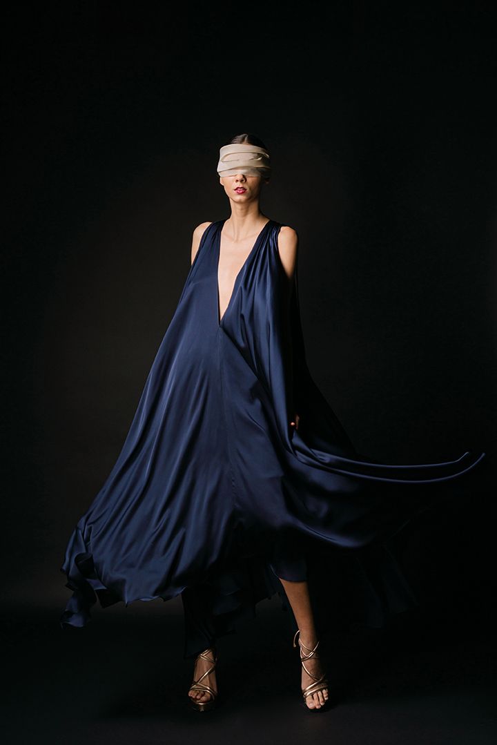 A dramatic fashion photo of a flowing navy blue dress against a dark background.